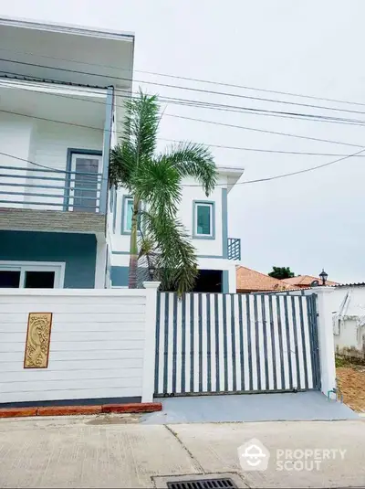 Modern two-story house with palm tree and gated entrance in suburban area.