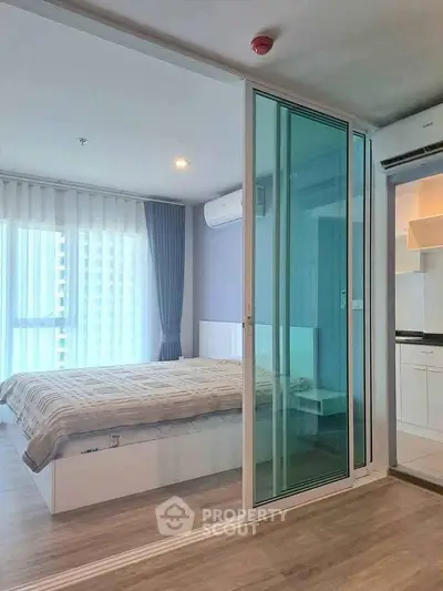 Modern studio apartment with glass partition, cozy bedroom, and compact kitchen in urban setting.