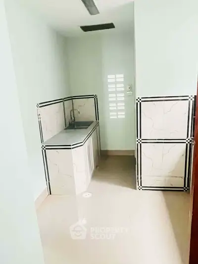 Compact kitchen area with tiled walls and stainless steel sink in a minimalist design.