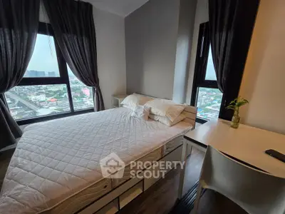 Modern bedroom with large windows offering stunning city views, featuring a cozy bed and sleek desk.