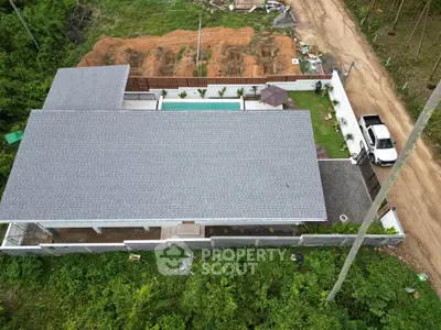 Aerial view of modern house with pool and garden in lush green setting.