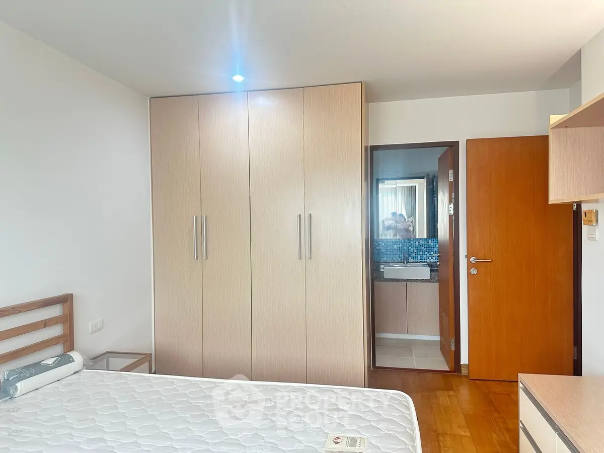 Spacious bedroom with wooden flooring and built-in wardrobe in modern apartment.