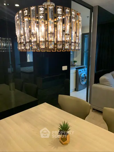 Modern dining area with elegant chandelier and view into a stylish living room with washing machine.