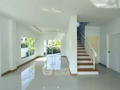 Spacious modern living room with staircase and large windows offering natural light and garden view.