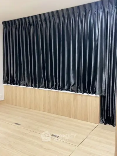 Spacious room with elegant floor-to-ceiling curtains and sleek wooden flooring, perfect for modern living.