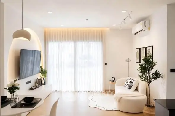 Modern living room with stylish decor, large TV, and natural light through sheer curtains.