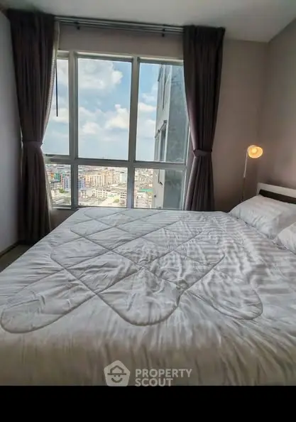 Spacious bedroom with large window offering stunning city view, perfect for urban living.
