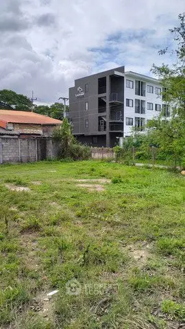 Vacant land with lush greenery and modern apartment building in the background, ideal for development.