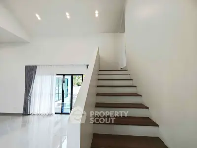 Modern minimalist staircase in a bright open-plan living area with large windows and sleek design.