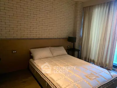 Cozy bedroom with brick accent wall and large window, perfect for relaxation.