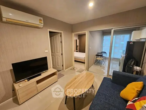 Modern living room with cozy sofa, TV, and sliding glass doors leading to a bright balcony.