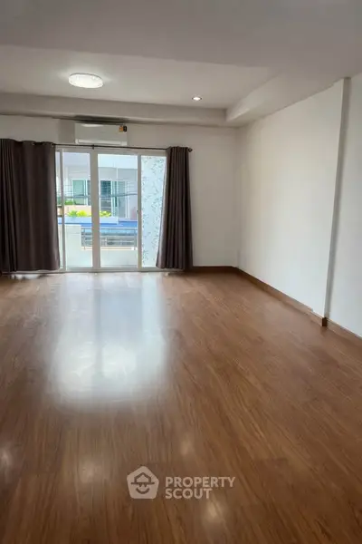 Spacious empty living room with wooden flooring and large windows.