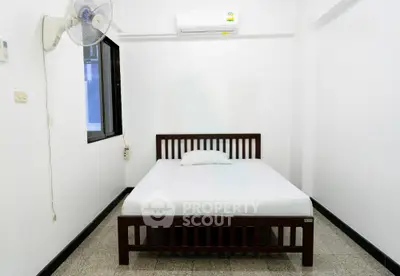 Minimalist bedroom with air conditioning and ceiling fan, featuring a simple wooden bed frame and white walls.