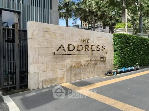 Elegant entrance of The Address with modern stone signage and lush greenery.