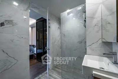 Modern bathroom with marble tiles and glass shower enclosure in luxury apartment.