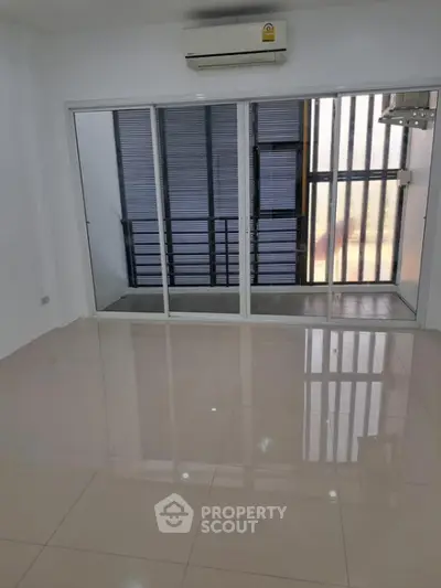 Spacious and well-lit living room with glossy tiled flooring and a large window with blinds, complemented by a modern air conditioning unit.