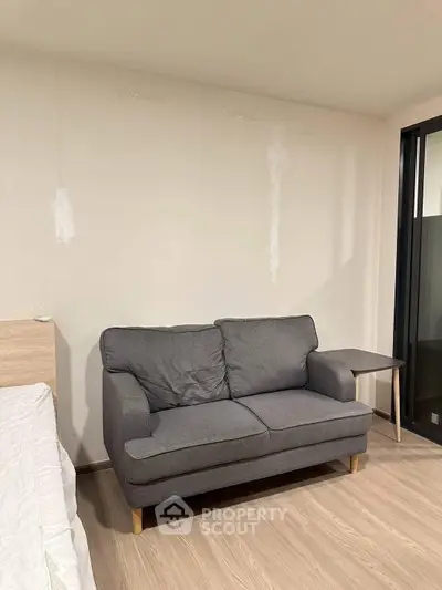 Cozy bedroom with modern gray sofa and wooden side table, perfect for relaxation and comfort.