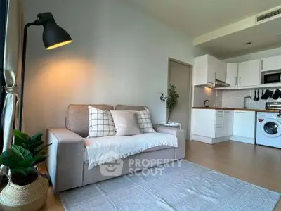Modern living room with cozy sofa and open kitchen featuring washing machine and stylish decor.