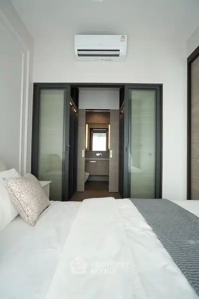 Modern bedroom with ensuite bathroom and air conditioning, featuring sliding glass doors and elegant decor.