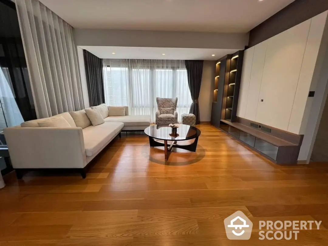 Spacious living room with polished hardwood floors, modern furniture, and ample natural light from large windows, perfect for relaxation and entertaining guests.