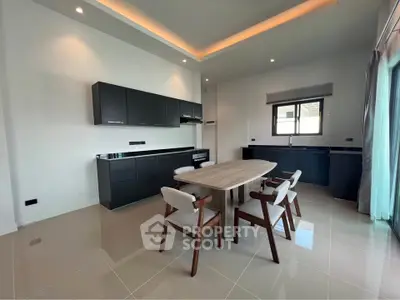 Modern kitchen with sleek black cabinets and dining area, featuring elegant recessed lighting.