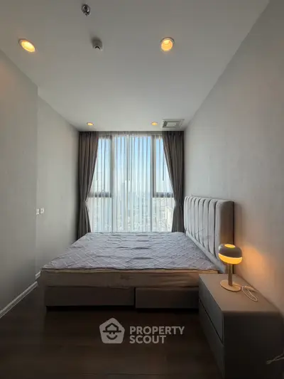 Modern bedroom with large window and city view, featuring stylish bed and nightstand.