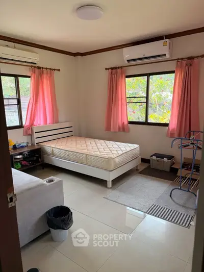 Cozy bedroom with natural light and air conditioning, featuring a single bed and pink curtains.