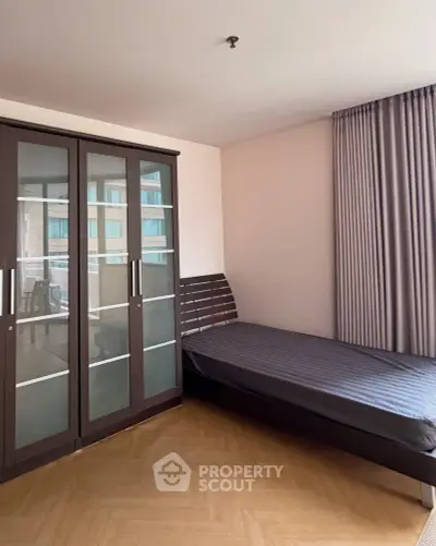 Spacious bedroom with modern wardrobe and single bed in a well-lit apartment.
