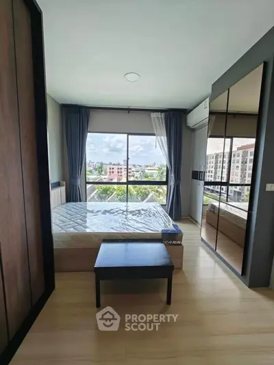Modern bedroom with large window offering city view, featuring sleek furniture and ample natural light.