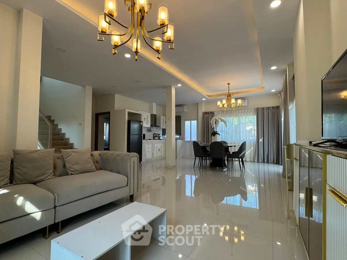 Luxurious open-plan living room with elegant chandelier and modern kitchen in a spacious home.
