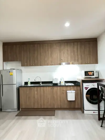 Modern kitchen with wooden cabinets, fridge, washing machine, and microwave in a sleek apartment.