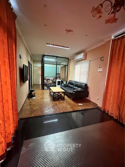 Spacious living room with modern decor and parquet flooring, featuring a cozy black leather sofa and large windows.