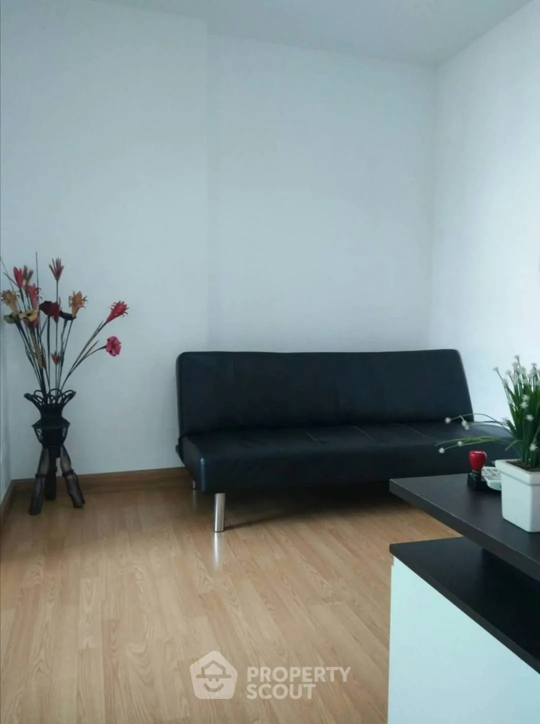 Modern minimalist living room with sleek black sofa and wooden flooring.