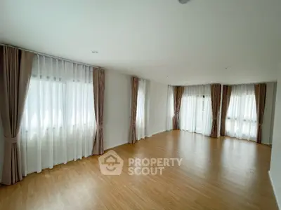 Spacious empty room with wooden flooring and large windows with elegant curtains