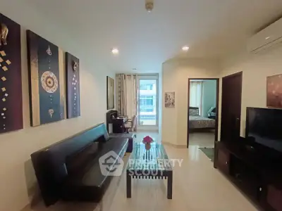 Modern living room with sleek black sofa, wall art, and flat-screen TV, leading to a cozy bedroom.