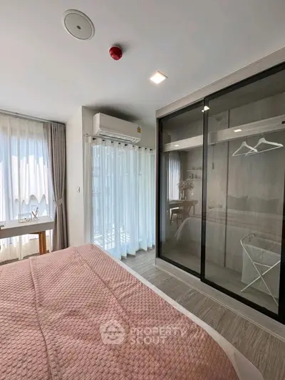 Modern bedroom with large windows and glass wardrobe doors, featuring stylish decor and natural light.