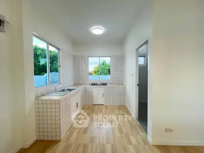 Modern kitchen with tiled walls and wooden flooring, featuring a gas stove and ample natural light.