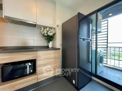 Modern kitchen with sleek appliances and balcony view, featuring a fridge, microwave, and washing machine.