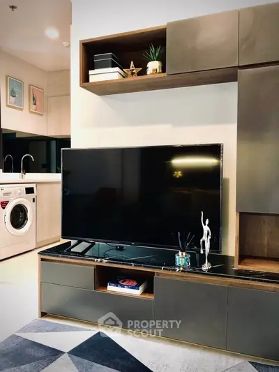 Modern living room with sleek TV unit and open kitchen featuring washing machine.