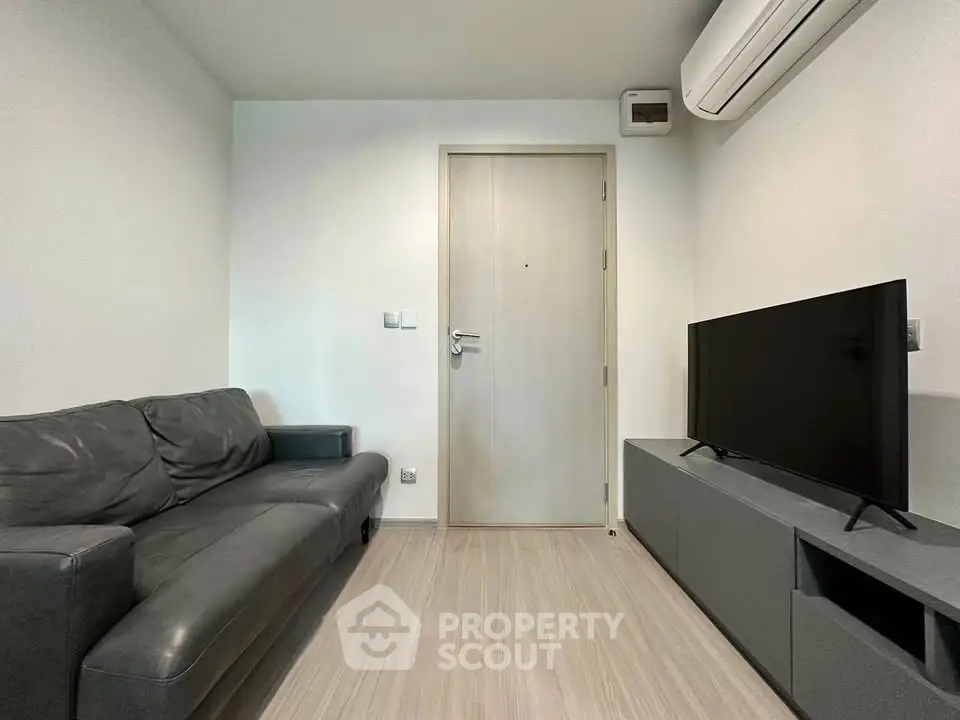 Modern living room with sleek black sofa and flat-screen TV, featuring minimalist design and air conditioning.