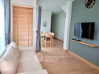 Modern living room with cozy sofa and wall-mounted TV, leading to a stylish dining area.