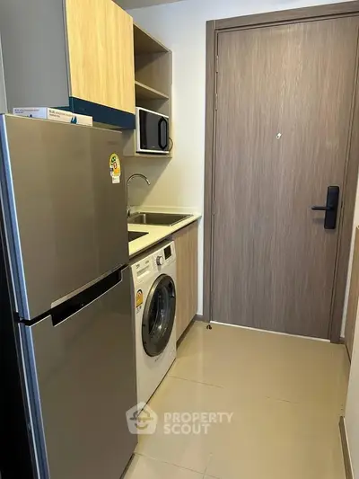 Modern compact kitchen with fridge, washing machine, and microwave in a sleek apartment.