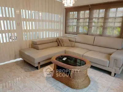 Stylish living room with beige sectional sofa and wicker coffee table, featuring elegant window blinds.