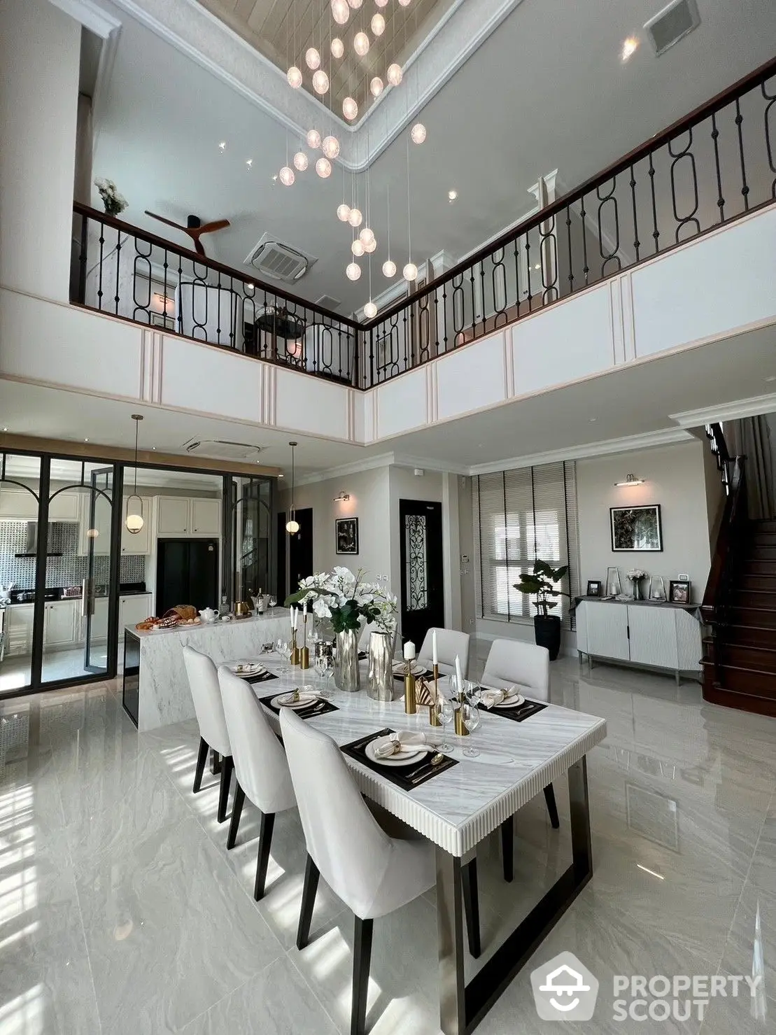 Luxurious double-height living room with elegant marble flooring, modern chandelier, and grand staircase leading to an upper-level balcony.