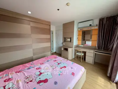 Cozy bedroom with wooden accents and built-in desk, featuring a playful pink bedspread.