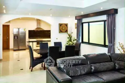 Spacious modern living room with open kitchen and dining area, featuring sleek black leather sofa and stainless steel appliances.