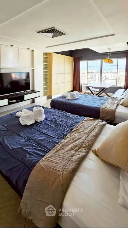 Spacious bedroom with twin beds and city view, modern decor and ample natural light.