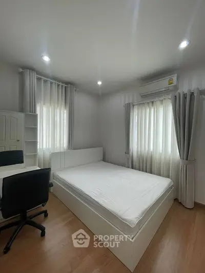 Modern bedroom with white furniture and natural light, featuring a desk and comfortable chair.