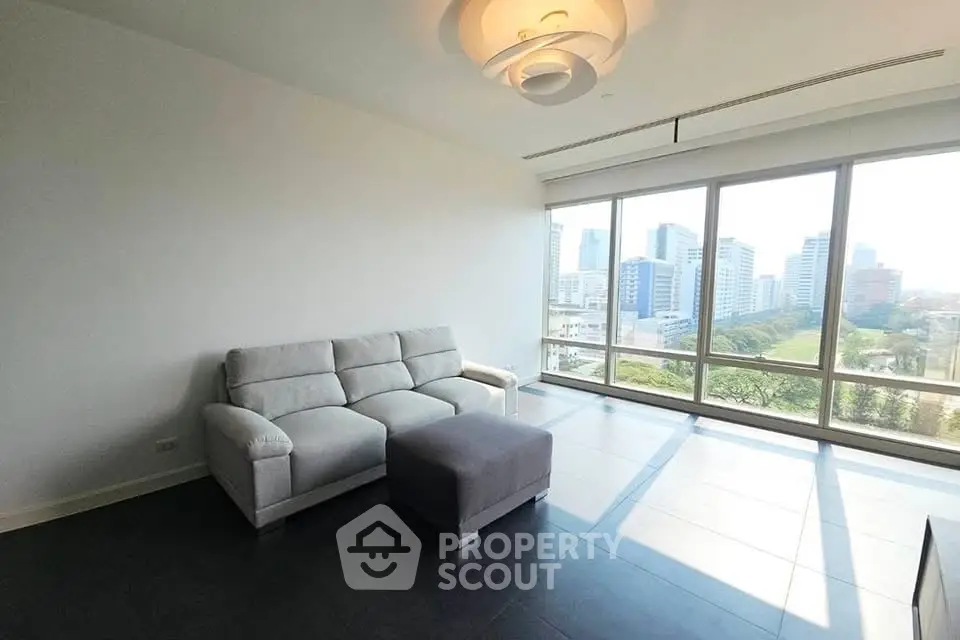 Spacious living room with modern sofa and panoramic city view through large windows.
