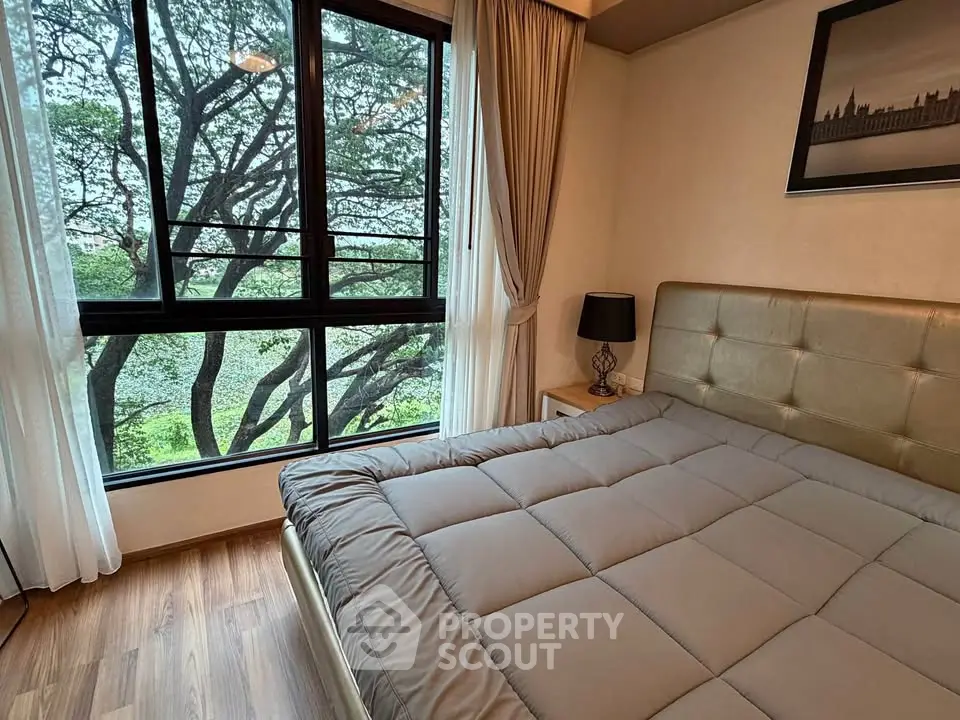 Cozy bedroom with large window offering serene tree views, featuring a plush bed and elegant decor.